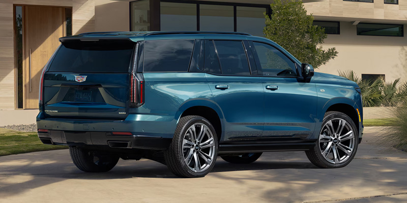 A teal Cadillac Escalade parked on a circular driveway in front of a modern luxury home