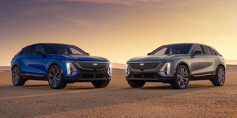 Two Cadillac SUVs parked in a desert landscape at sunset