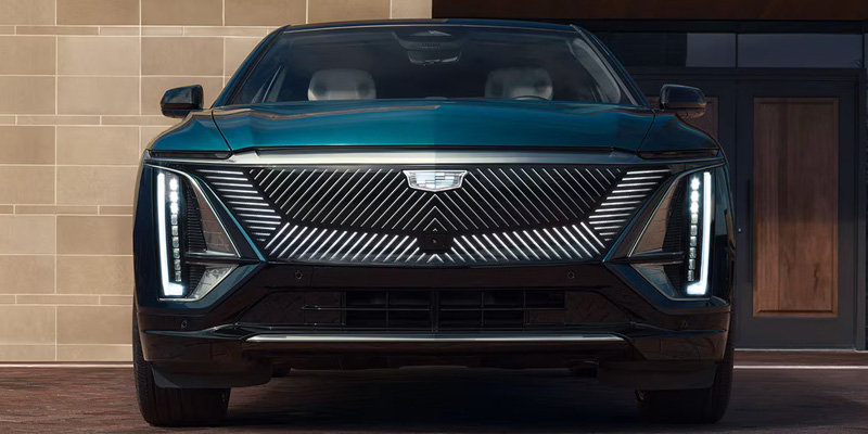 Front view of a dark teal Cadillac LYRIQ electric SUV showcasing its illuminated grille and vertical headlights.